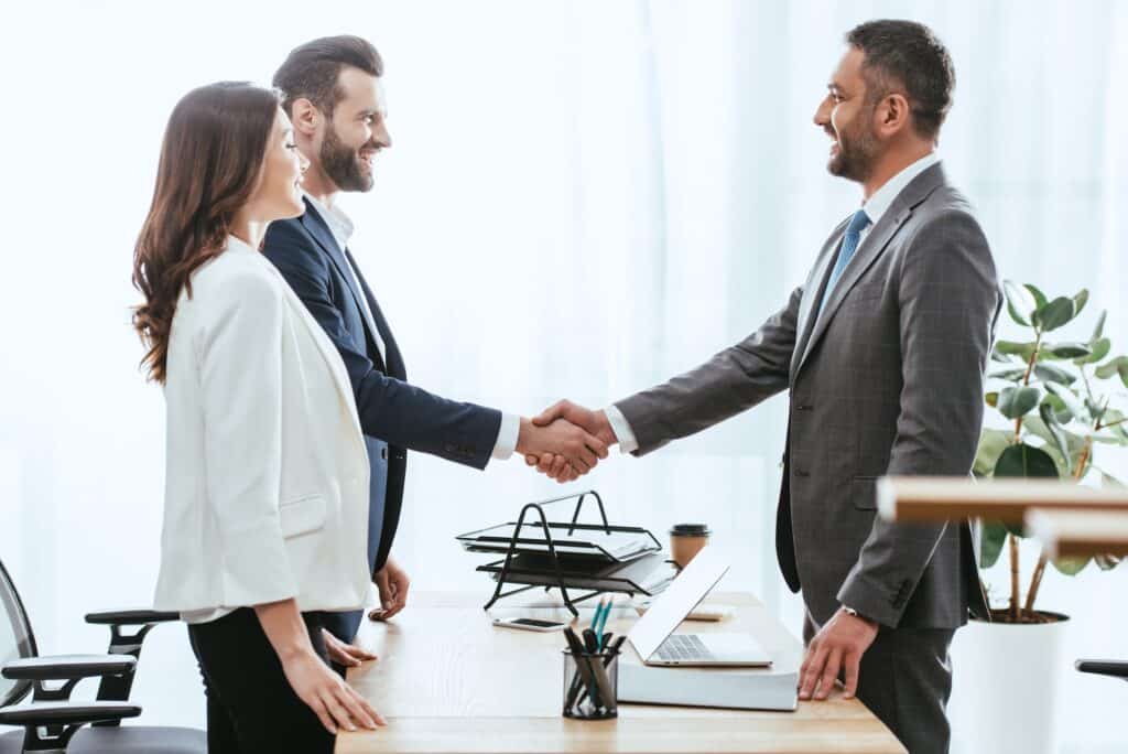 handsome advisor in suit shaking hands with investors at workplace
